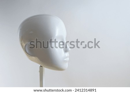 White neutral head of a mannequin figure in minimalist style on a metal stand against a light beige gray background, copy space, selected focus