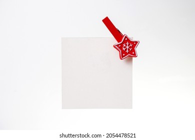 White Note With A Red Christmas Clothespin On A White Background.