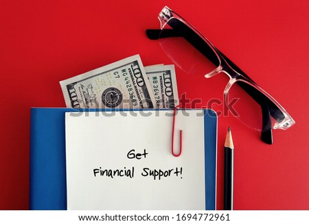 White note with text written GET FINANCIAL SUPPORT clip with notebook, dollars cash money and reading glasses - concept of corona covid 19 virus effect on retiree living expense or retirement planning