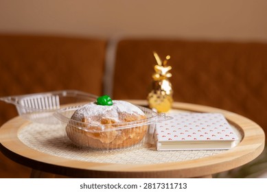 A white notebook decorated with small red hearts placed next to a powdered pastry in its open plastic packaging on a wooden surface.
