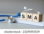white notebook, Medical stethoscope and wooden blocks with the medical abbreviation SMA for spinal muscular atrophy, severe genetic disease, Beautiful gray background, Medical concept