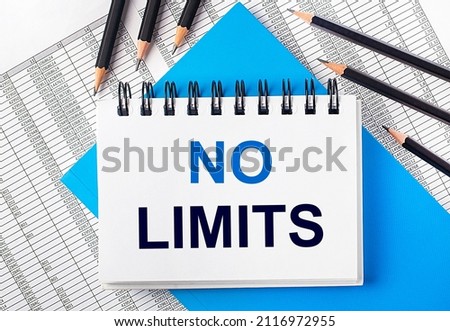 White notebook with the text NO LIMITS on the table next to black pencils on a blue background and reports. Business concept