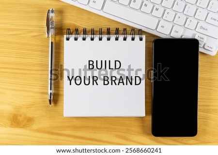 White notepad with text Build Your Brand lying on laptop on wooden table. Marketing business concept