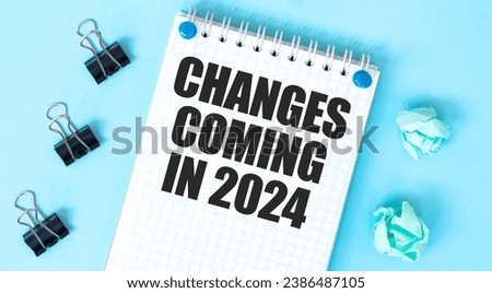 White notepad with text CHANGES COMING IN 2024 and office tools on the blue background