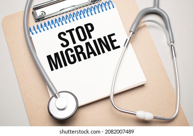 White notepad with the words STOP MIGRAINE and a stethoscope on a blue background. Medical concept