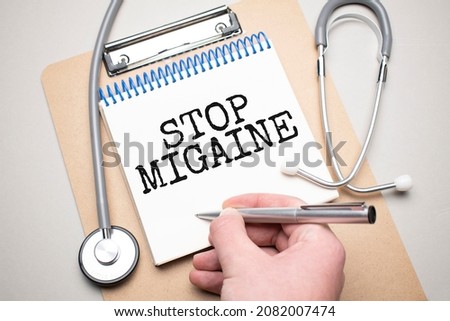 White notepad with the words STOP MIGRAINE and a stethoscope on a blue background. Medical concept