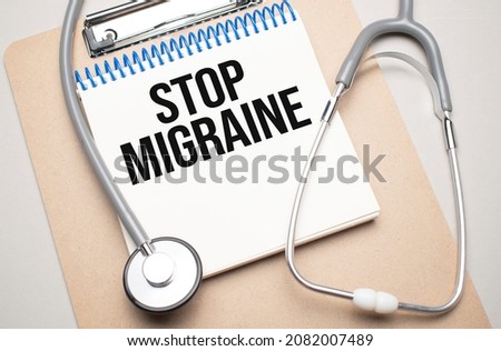 White notepad with the words STOP MIGRAINE and a stethoscope on a blue background. Medical concept