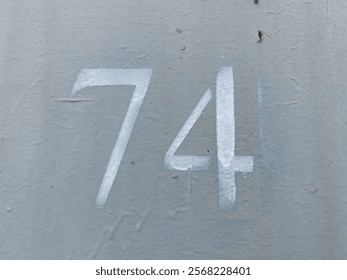 White number 74 on gray background. Seventy-four on textured surface 