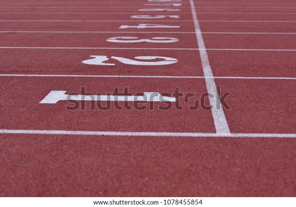 White\
numbers on starting line of a running track field, 1-8, with\
straight white lines divided each track\
equally.