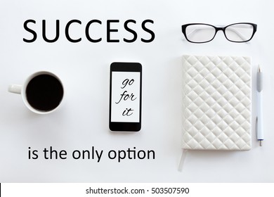 White office desk with glasses, mobile phone, coffee and pen on it. Lady office supply. Top view. Motivational text "Success is the only option"