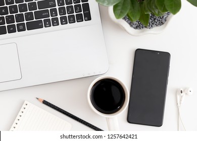 White office desk with laptop, coffee, mobile phone, notebook with pen. Top view with copy space, flat lay