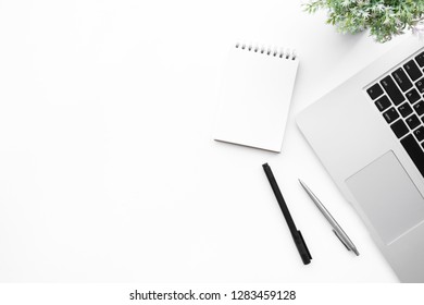 White office desk table with blank notebook page with pen and laptop computer. Top view with copy space, flat lay.