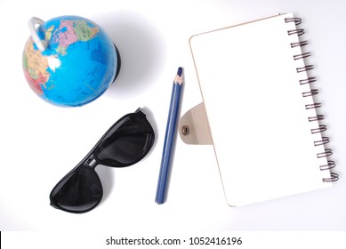 White Office Desk Table With Open Note Book, Color Pencil Globe, And Sun Glasses . Top View With Copy Space, Flat Lay.