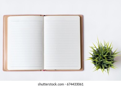 White Office Desk Table With Open Diary, Glass And Plant. Top View With Copy Space, Flat Lay.