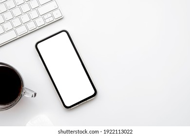 White Office Desk Table With Smartphone With Blank Mockup Screen, Cup Of Coffee And Computer Keyboard. Top View With Copy Space, Flat Lay.
