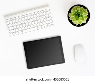 White office desk table with tablet pc computer in ipade style with black screen, wireless aluminum keyboard, mouse and succulent flower in pot. Top view with copy space. Flat lay.