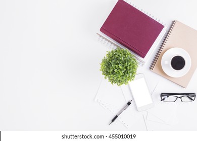 White Office Desktop With Blank Smartphone, Glasses, Coffee Cup, Spiral Notepads, Book, Decorative Plant And Other Items. Top View, Closeup, Mock Up