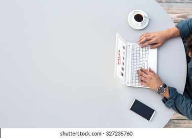 White Office Round Table And Man Working On Computer Top View Casual Clothing Typing On Keyboard With Marketing Chart On Screen Smart Phone And Cup Of Coffee Aside