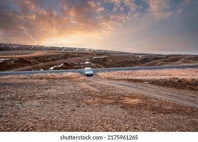 White offroad van moving on road. Scenic view of landscape against cloudy sky in valley. Vehicle used for off-road pathway in northern Alpine region during sunset.