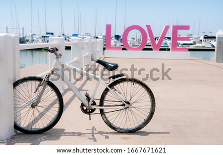 White old  bicycles parked in row of stand bike parking rack on the bridge of Yacht harbor and there is a pink letter on the word love behind, Bicycle parked in row of stand bike parking rack.