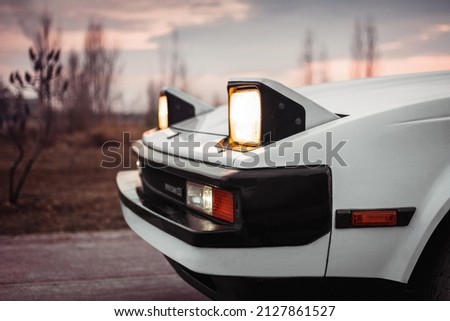 White old japanese 1980s car with pop-up headlights. Blurry countryside in the background