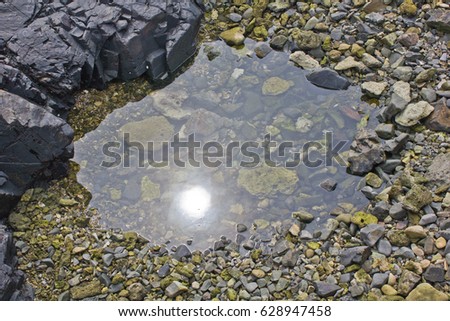 The white orb of the sun is reflected in the mirror surface of a rocky tidal pool at low tide on the Pacific Ocean coast of Japan.