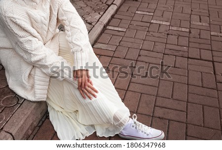 white oversized sweater, light skirt and white sneakers. Details of women's street-style clothing.