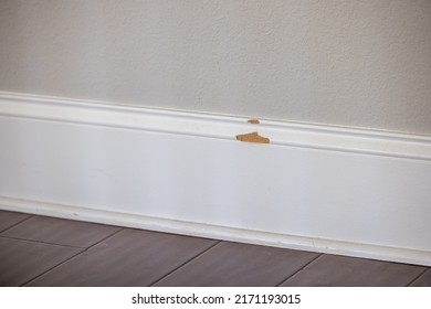 The White Painted Baseboard Trim On A New Construction House That Has A Broken Chunk Missing From The Mdf Material That Needs Repair.