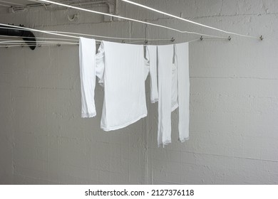 White Pajamas Or Clothing Hanging From Drying Lines Inside Communal Laundry Room Inside Apartment Building. No People.