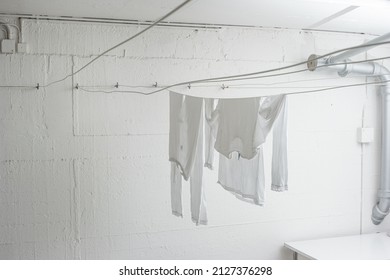 White Pajamas Or Clothing Hanging From Drying Lines Inside Communal Laundry Room Inside Apartment Building. No People.