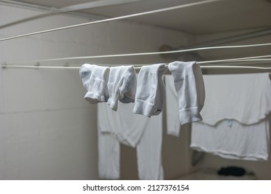 White Pajamas Or Clothing And Short Socks Hanging From Drying Lines Inside Communal Laundry Room Inside Apartment Building. No People.
