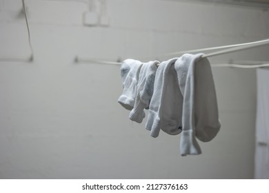 White Pajamas Or Clothing And Short Socks Hanging From Drying Lines Inside Communal Laundry Room Inside Apartment Building. No People.