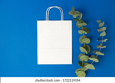 White Paper Bag With Handles And Eucalyptus Leaves On Blue Background. Flat Lay Banner, Top View, Copy Space, Zero Waste, Plastic Free Items. Mockup Eco Package