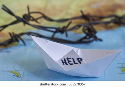 White paper boat onto world map with "Help" sign on it and barbed wire.