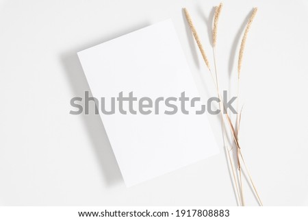 White paper empty blank, dried grass decoration on white background. Invitation card mockup on white table. Flat lay, top view, copy space, mockup