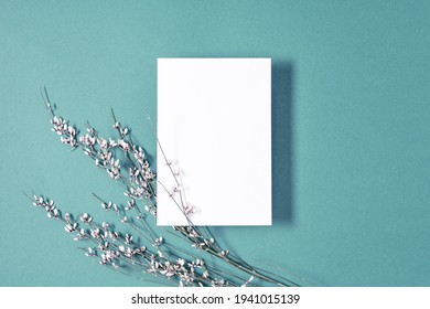 White paper empty blank, flowers on blue background. Invitation card mockup on white table. Flat lay, top view, copy space, mock up