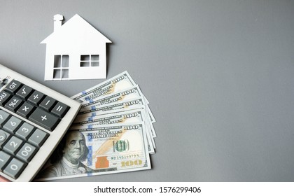 White paper house with dollars banknotes and calculator on a grey background. Concept of save, investment in real estate, refinance, retention, collect money for buy, sell, decorate or repair for home - Shutterstock ID 1576299406
