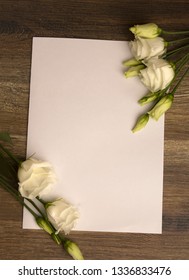 White paper layout with white eustoma flowers on wooden background.