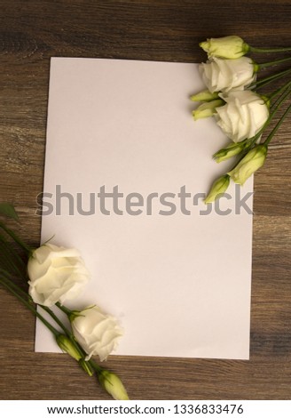 White paper layout with white eustoma flowers on wooden background.
