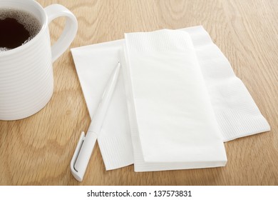 White Paper Napkin On Wooden Table With Pen For Making Notes, And Mug Of Coffee, Ideal For Noting Down Phone Numbers, And That Great Idea You Had At The Coffee Shop.