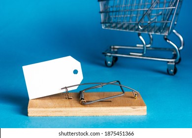 White paper plate in a wooden mousetrap on a blue background. Supermarket cart in the background. Marketing gimmicks. Consumer deception. Place for your text. - Shutterstock ID 1875451366