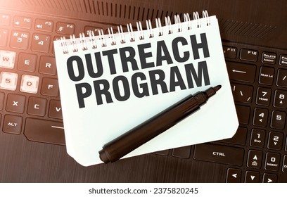 White paper sheet with text OUTREACH PROGRAM on the black laptop