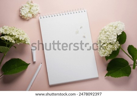 White paper spiral notebook with  hydrangea flowers on a soft beige background.Top view, flat lay. Copy space.