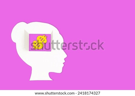 White paper-cut female head, set against a vibrant pink backdrop, features a window in the brain area revealing a golden dollar sign. Mindful approach to personal and financial decision-making.