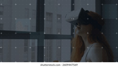 White particles moving over grid network against caucasian woman wearing vr headset at home. computer interface and technology concept