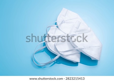 White particulate foldable protective masks with elastic ear loops on bright blue background. Essential personal protective equipment for health and safety.