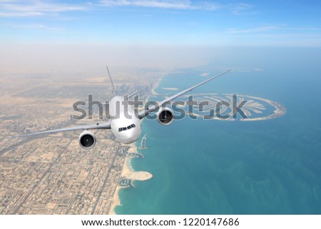White passenger airliner flying over Dubai city and sea coastline