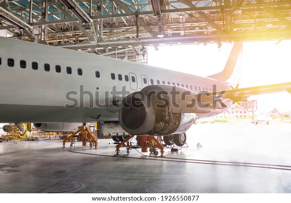 White passenger airliner under maintenance in\
the hangar. Repair of jet plane engine on the wing and checking\
mechanical systems for flight\
operations