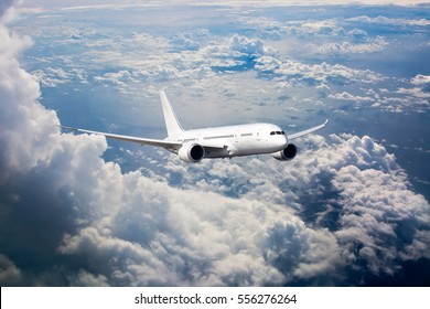 White passenger jet plane in the blue sky. Aircraft flying high through the cumulus clouds. Airplane front view.