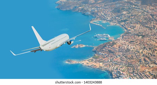 White passenger jet plane in the sky - Aircraft flies high over the city and and sea coast in the background Kusadasi port and cruise ship - Kusadasi